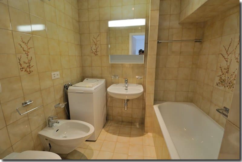 Bathroom with bathtub, sink, bidet, toilet, mirror, washing machine, tiles