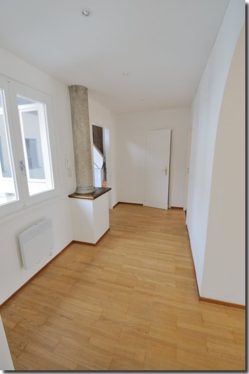 wide hallway, wooden floors, large windows, visible interior column, white walls, door at end