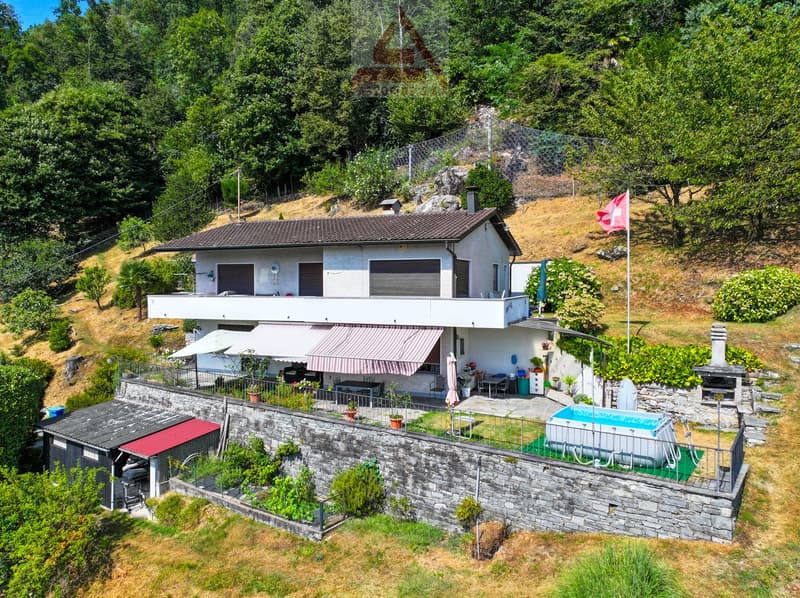 2-story house with a balcony, surrounded by lush greenery and a swimming pool in the backyard. The house has a stone wall and a red and white exterior.