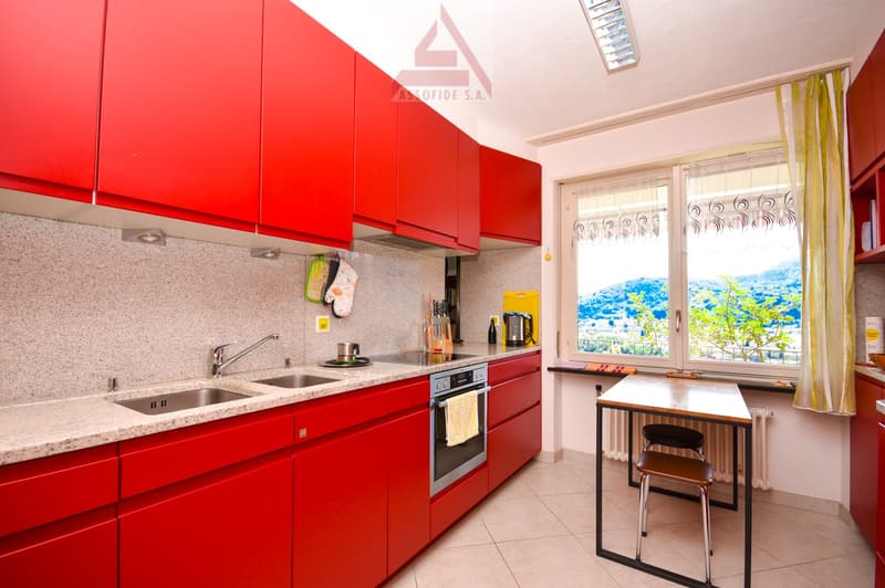 Spacious kitchen with red cabinets, granite countertops, sink, oven, and a small dining table with chairs. Large window overlooking the outdoor scenery.