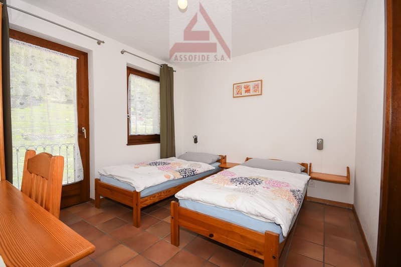 Two twin beds, wooden furniture, tiled floor, large windows with curtains, Assofide S.A. logo on the wall