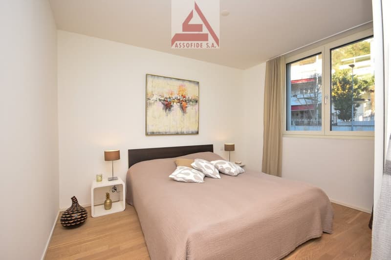 Spacious bedroom with large windows, hardwood floors, a king-size bed, bedside tables, and a decorative painting on the wall.