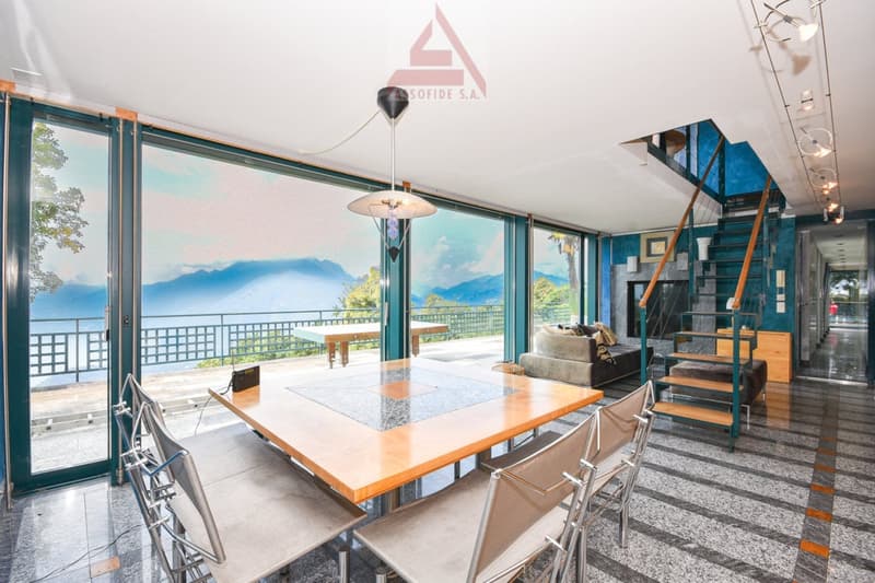 Spacious living area with large windows offering a scenic view of the mountains, wooden dining table, modern furniture, and a staircase leading to an upper level.