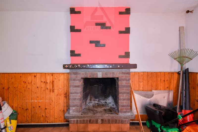 Brick fireplace with a large red abstract artwork above it, wooden paneled walls, various household items and tools in the room