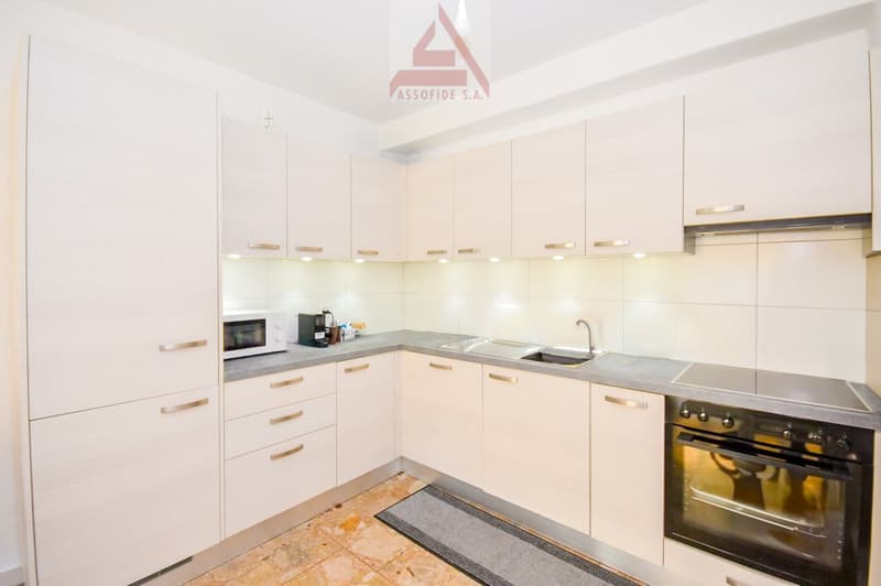 White cabinets, marble countertops, oven, microwave, sink, grey floor mat, light tiled flooring