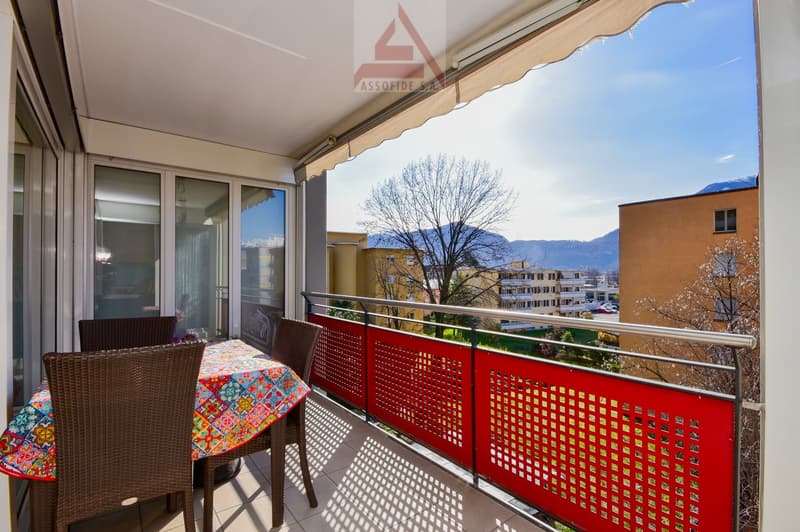 Balcony with view of the mountains, table and chairs, red railing, awning