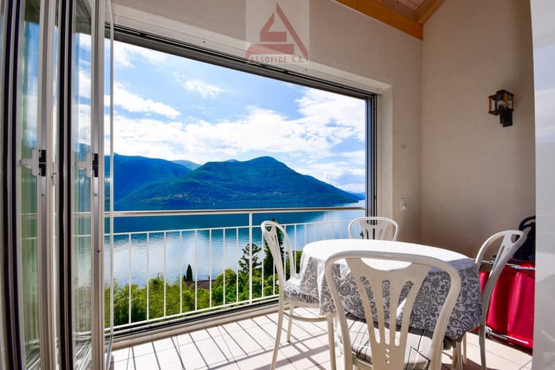 Sliding doors opening to balcony, outdoor dining table with chairs, view of lake and mountains