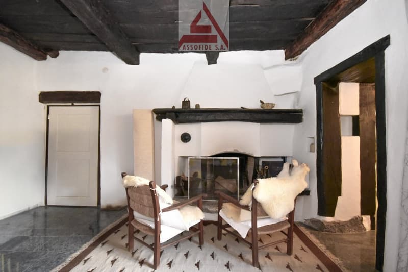Wooden beams, white walls, tile floor, fireplace, wooden armchairs, rug