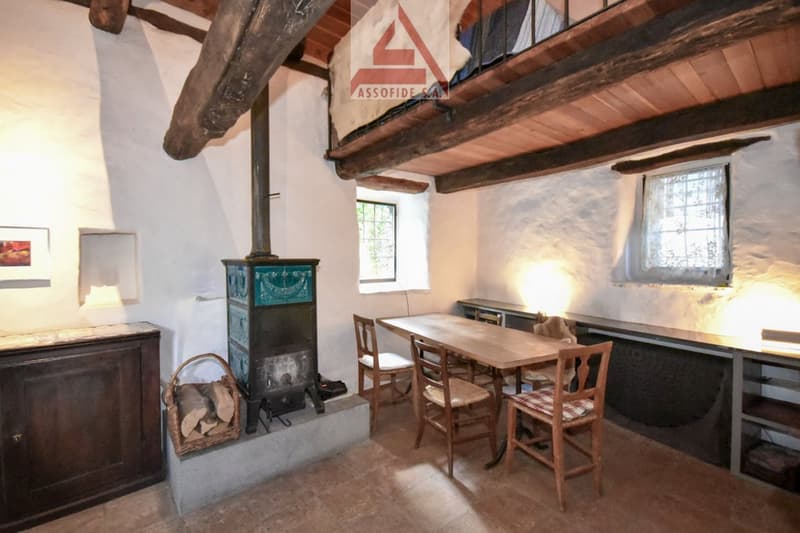 A fireplace and a dining table with chairs, a wooden cabinet, and wooden beams on the ceiling