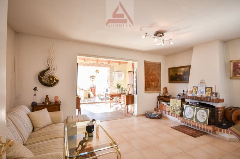 living room with tile floor, large fireplace, a couch, coffee table, side tables, lamps, artwork on the wall, hallway leading to dining room with a table and chairs
