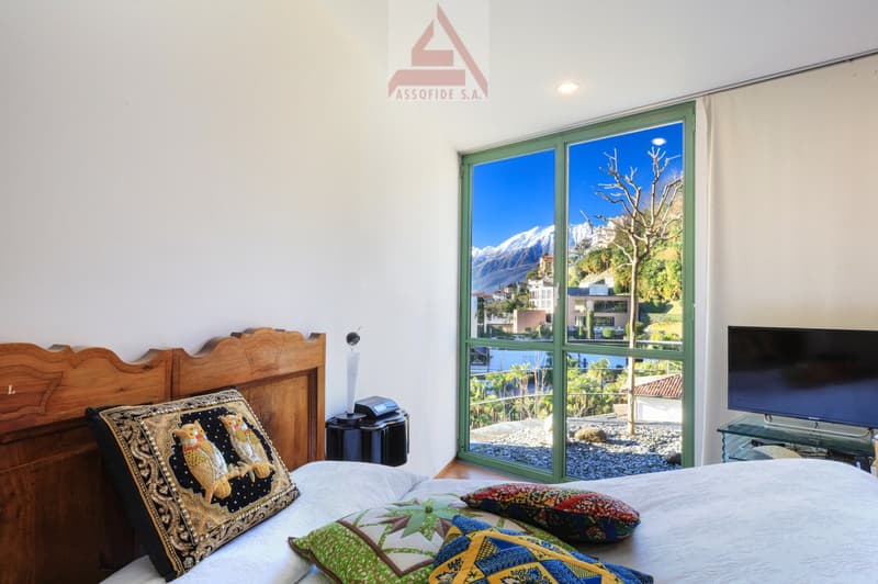 large glass window, mountain view, bed with pillows, night stand, television