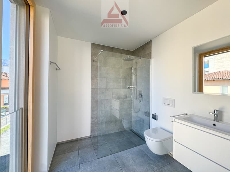 modern bathroom with gray tiles, glass shower enclosure, white vanity, toilet, silver faucet