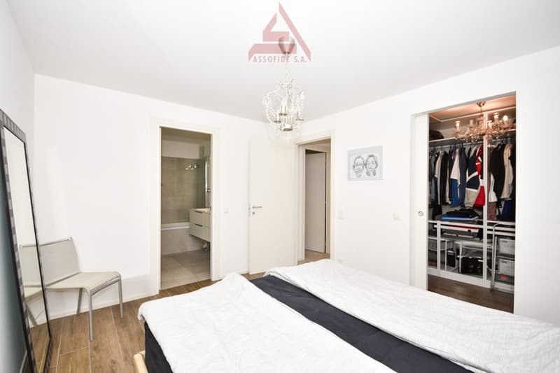 large bed, white and black sheets, chair, mirror, closet with many clothes, chandelier, picture