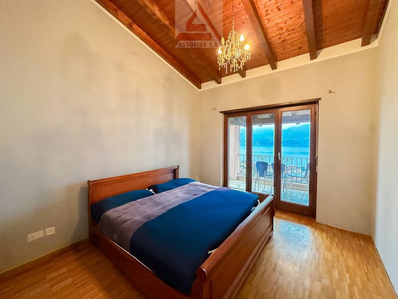 large wooden bed with blue bedspread, glass doors leading to balcony, wooden ceiling with chandelier, wooden floor, white walls