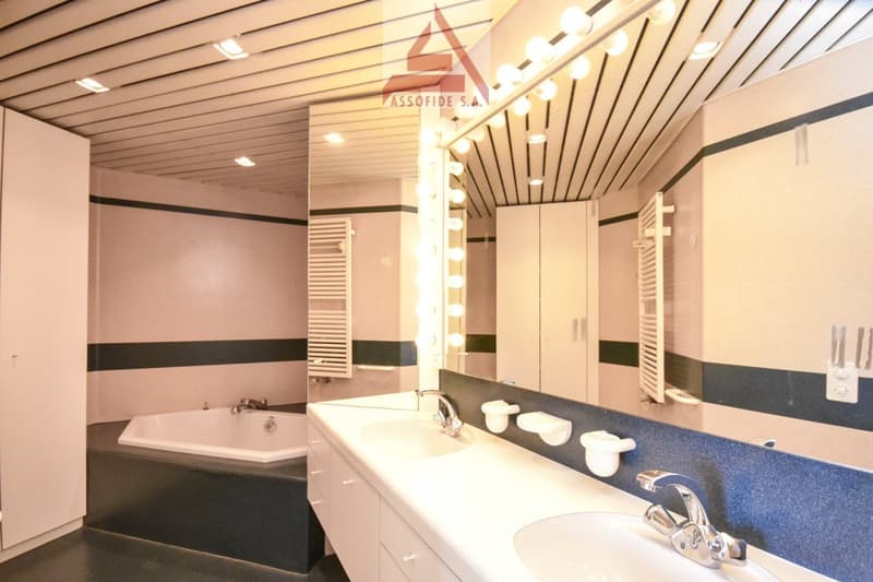 Bathroom with double sink, bathtub, mirror with lights, built-in cabinets, towels rack, white wall and flooring.