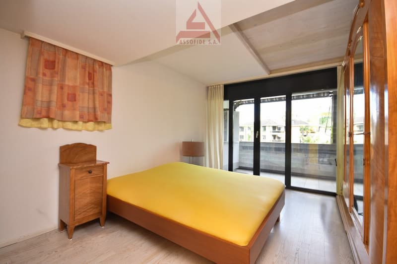 Bedroom with wooden bed, yellow sheets, wooden nightstand, large window with curtains, balcony