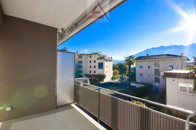 Balcony with metal railing, view of nearby buildings and mountains in the distance