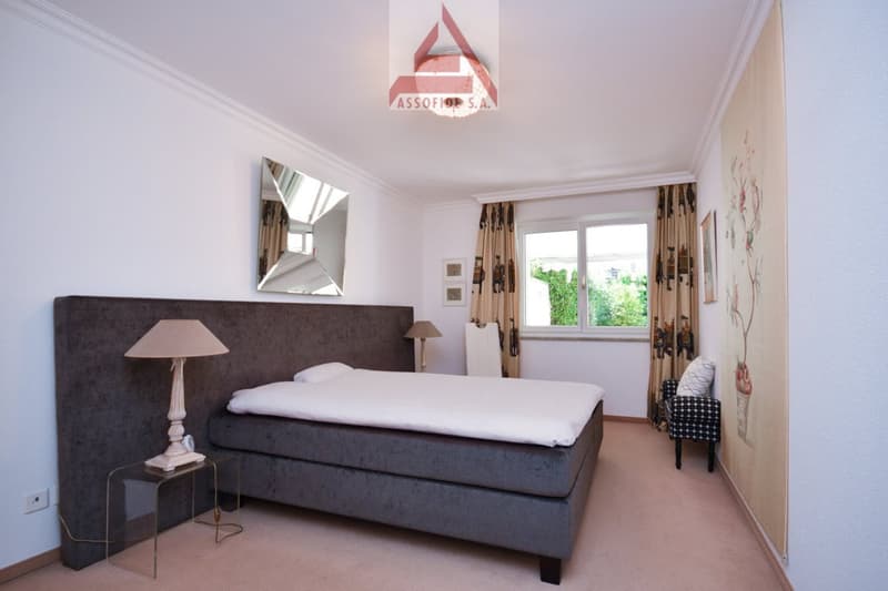 Modern bedroom with gray bed, lamp, mirror, curtains, painting, outlet, bedside table, and white sheet