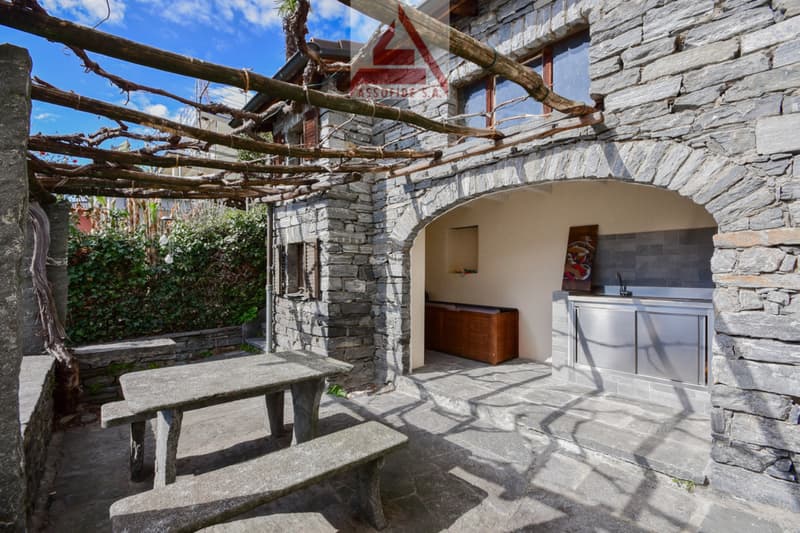 Stone built exterior with tables, chairs, and a wooden chest in a niche.