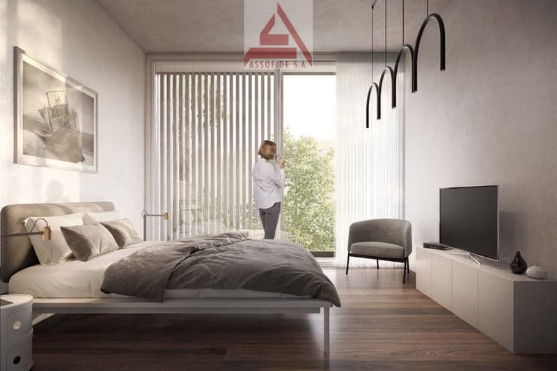 A bedroom with bed, pillows, flat screen tv, chair, and woman standing on a balcony looking outside.