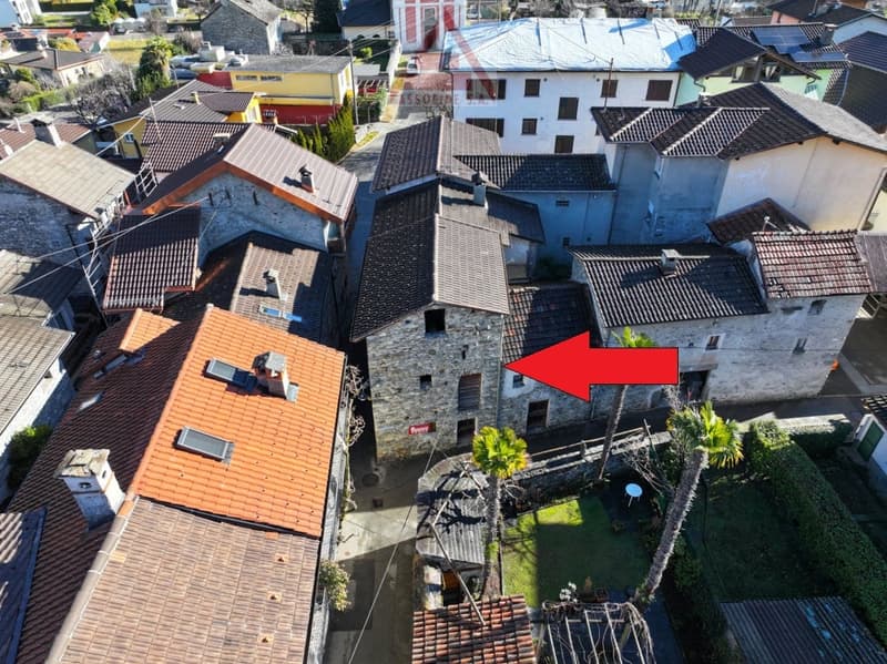 Stone house, terracotta roofs, multiple levels, narrow streets, surrounded by greenery, indicated by red arrow