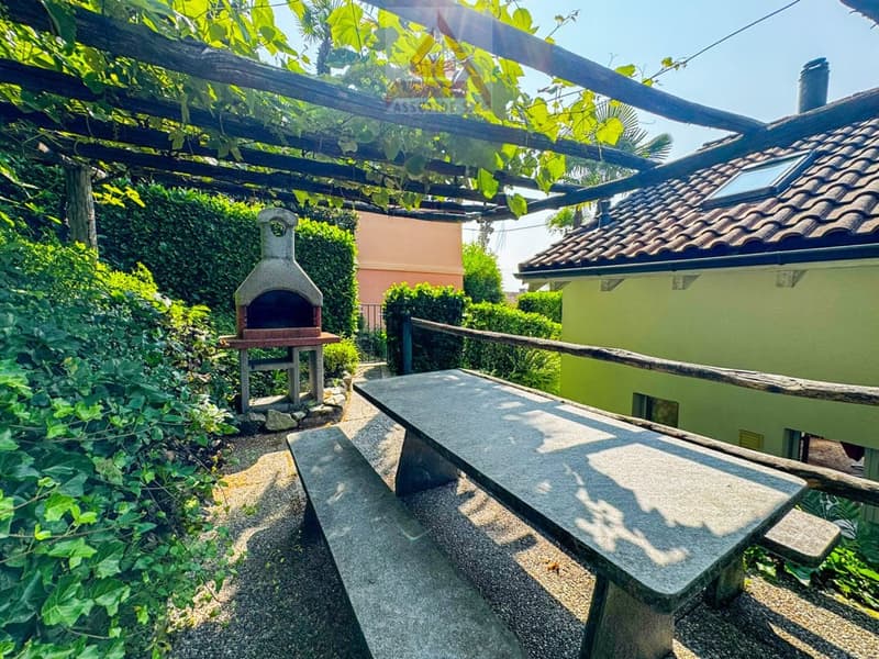 Garden with wooden table, wooden bench, pergola, outdoor grill, hedge, house in the background