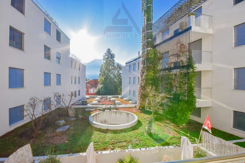 White modern building, multiple floors, multiple balconies, a garden with plants and rocks