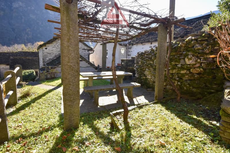 pergola with table and benches, stone wall, greenery, mountain in the distance
