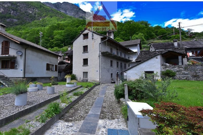 Collection of traditional stone houses with stone paths, greenery, a distant mountain view