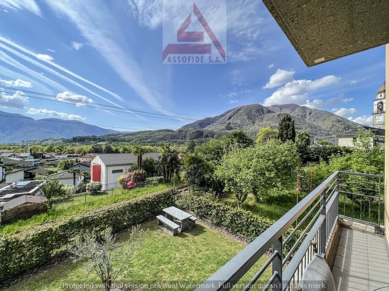 balcony with railing, table and benches, green grass, bushes, mountains in the distance