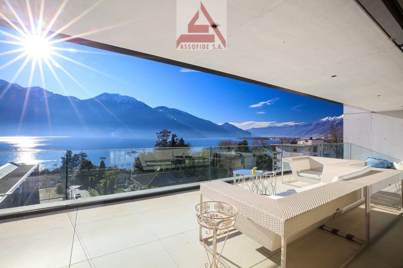 Balcony with glass railing, white furniture, table, chairs, view of mountains and lake