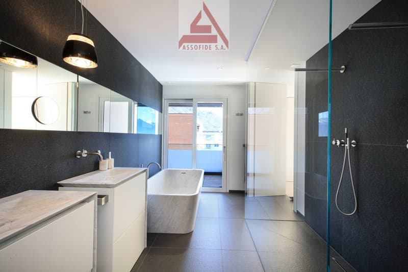 modern bathroom with white bathtub, large mirror, glass shower, white cabinets, marble countertops, black tiles