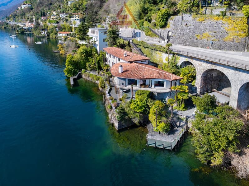 House on the lake, red roof, white walls, surrounded by trees, bridge in the background