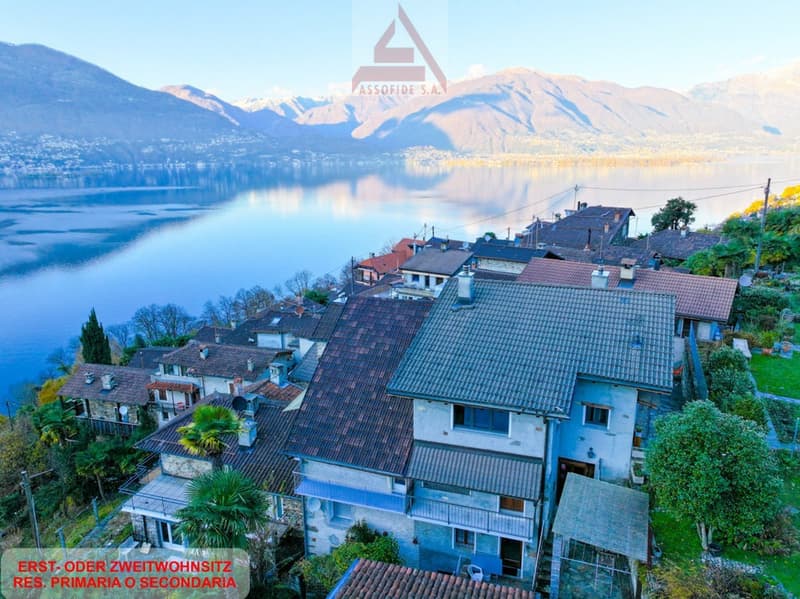 Houses with tiled roofs, surrounded by greenery, mountains and a lake in the background