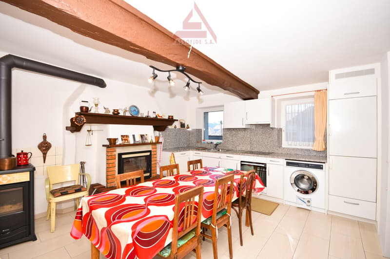 Dining room with a fireplace, a dining table, chairs, a washing machine, and a kitchen area with a sink and a stove