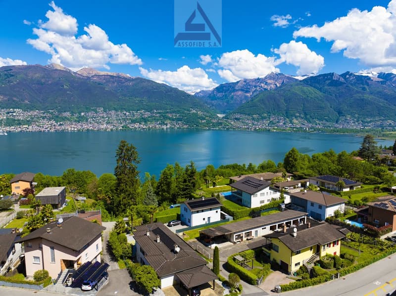 Aerial view of a residential area with several houses, solar panels, and a lake in the background
