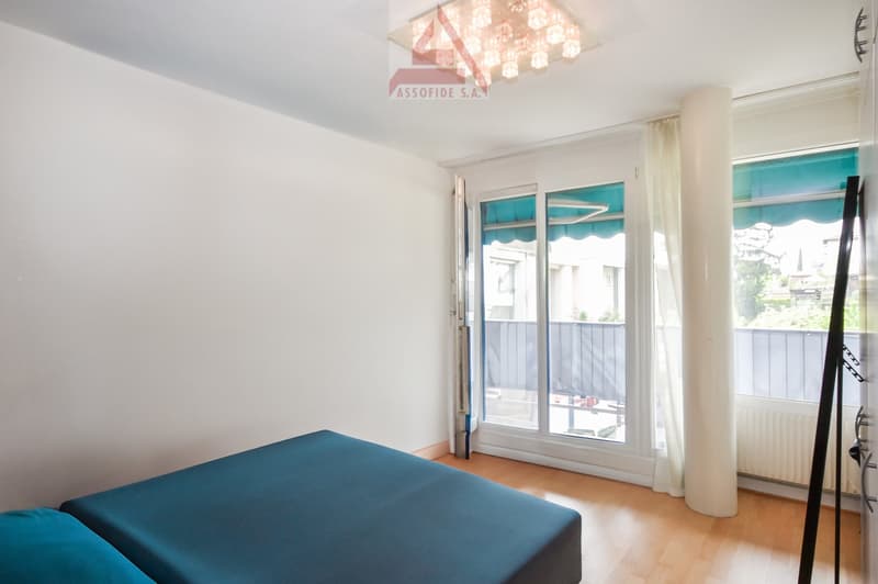bedroom with double bed, sliding glass door to balcony, wooden floor, white walls, ceiling light