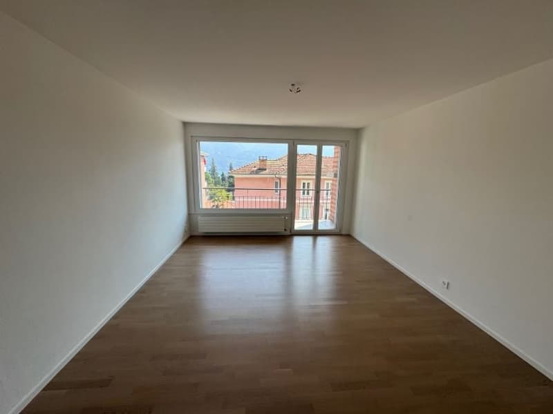 empty room, white walls, wooden floor, large glass door leading to a balcony with railings, mountain view