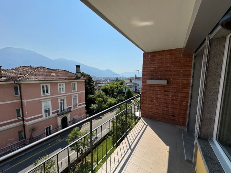 Brick building with a balcony overlooking a city street and mountains.