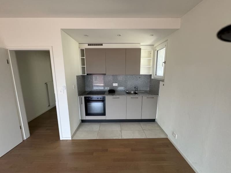 Empty kitchen with tiled floor, white walls, cabinets, stove, sink, faucet, small window, electric outlet