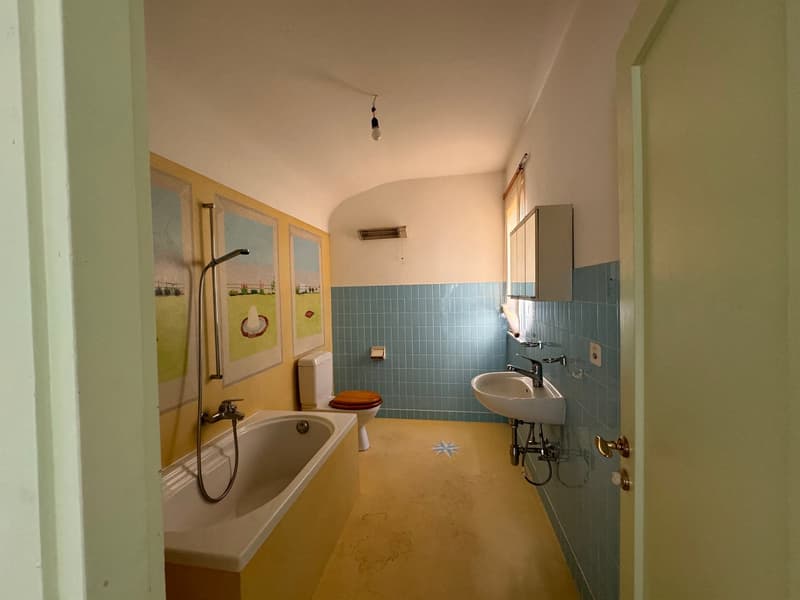 Bathroom with a bathtub, sink, and tiled walls. The room has a private washing machine and some artwork on the walls.