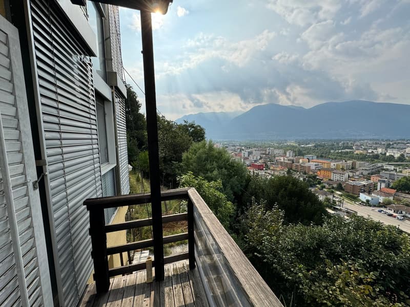 Wooden balcony with a view of a city surrounded by mountains and trees