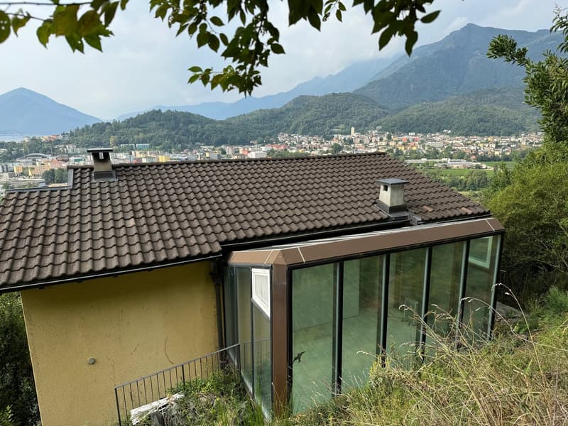 Two-story house with a tiled roof, large windows, and a balcony or terrace overlooking a mountainous landscape with a town in the distance.
