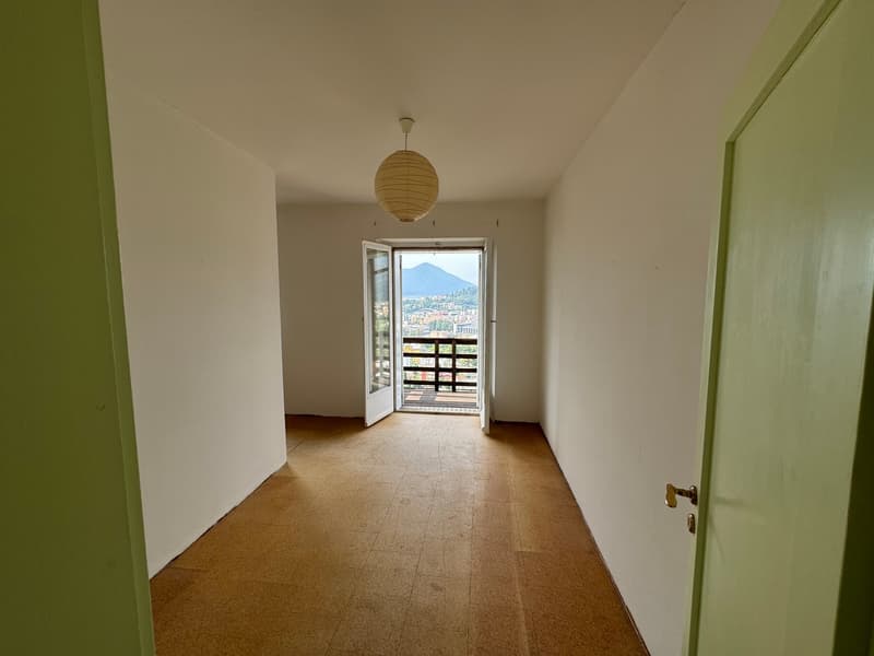Hallway with white walls, tiled floor, and a balcony door leading to a view of the city and mountains.