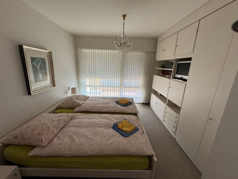 Twin bedroom with two single beds, lamp, picture frame, cabinet with TV, chandelier