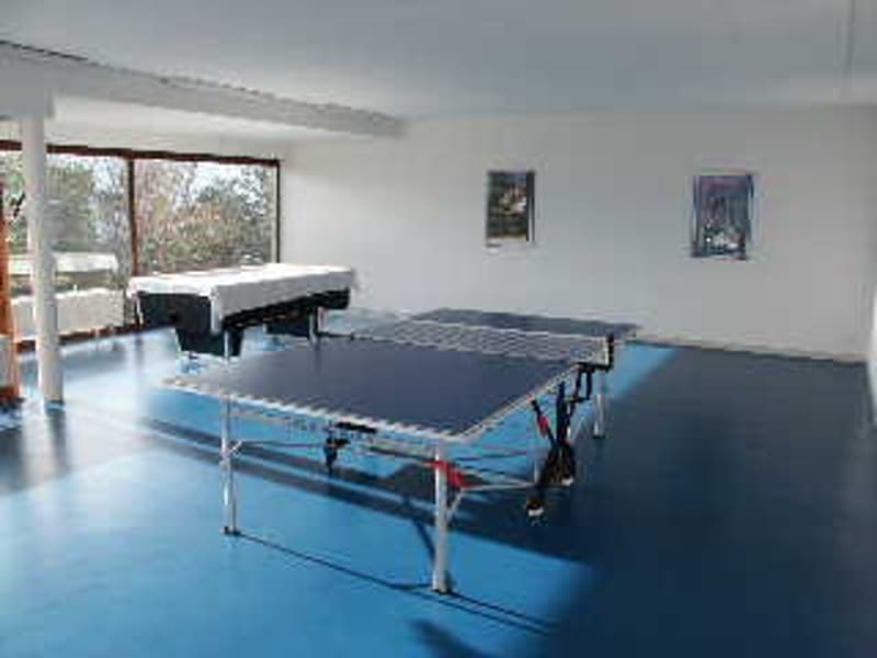 Indoor ping pong table setup, room has white walls, large windows, blue floor