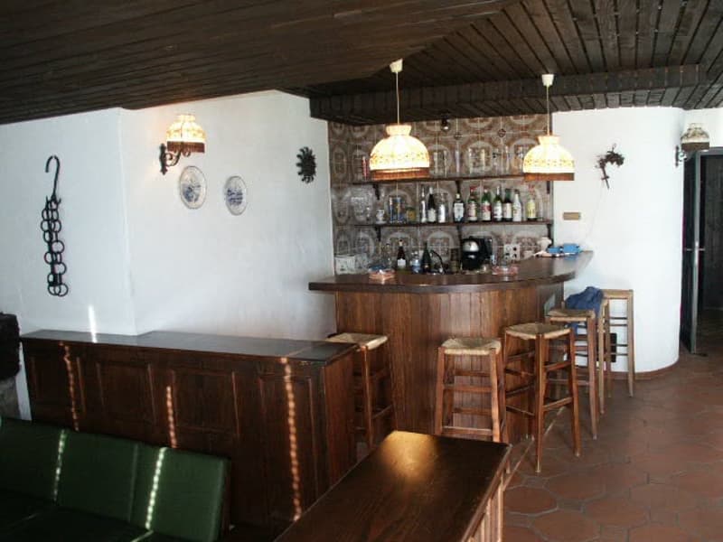 A wooden counter with stools, shelves stocked with bottles, a coffee maker, and lamps.