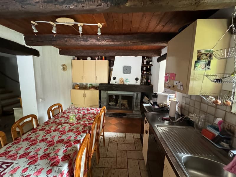 Dining room with a table and chairs, a fireplace, wooden cabinets, and a kitchen area with a sink and a stove
