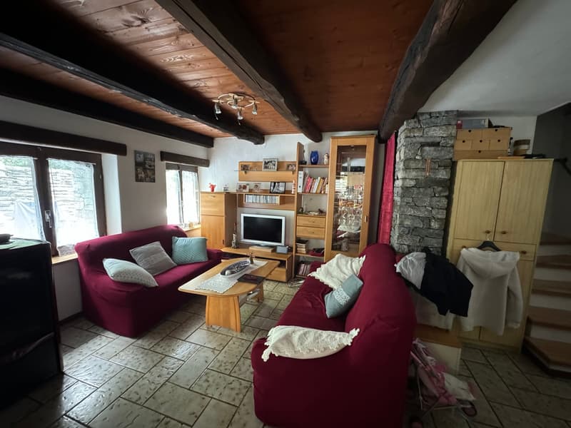 wooden ceiling, red couches, coffee table, TV, wooden shelves, stone wall, tiled floor