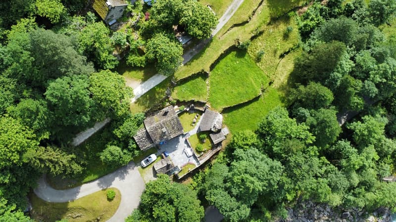 Stone house, gravel driveway, car parked, surrounded by trees, green lawn